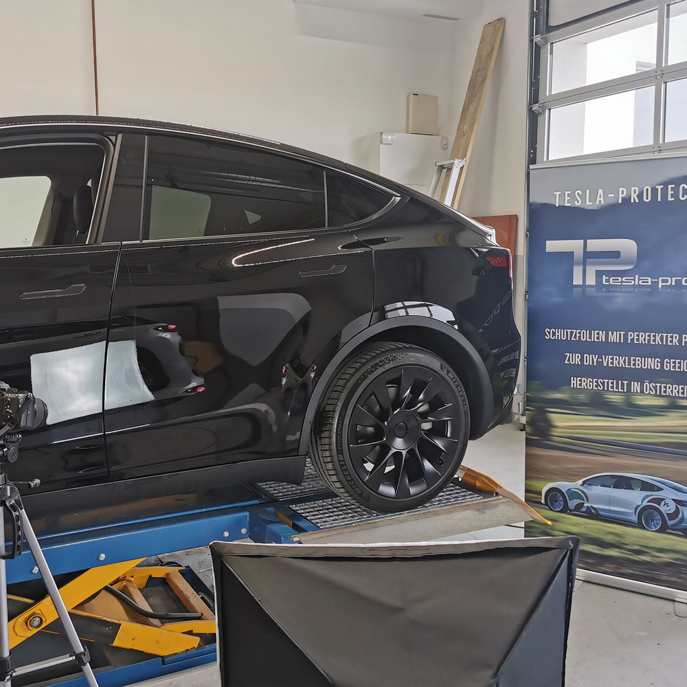 Tesla Model Y nera sul ponte sollevatore davanti a uno striscione Tesla-Protect
